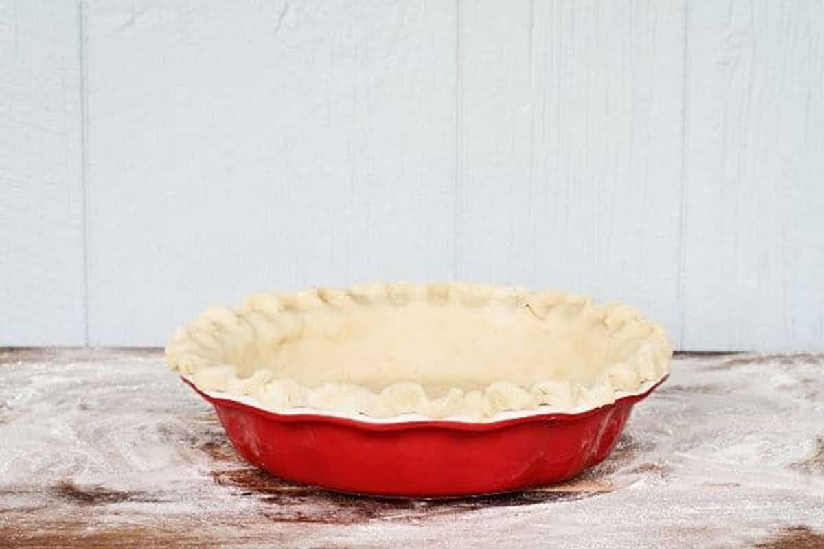 A pie crust in a red pie pan ready to bake.