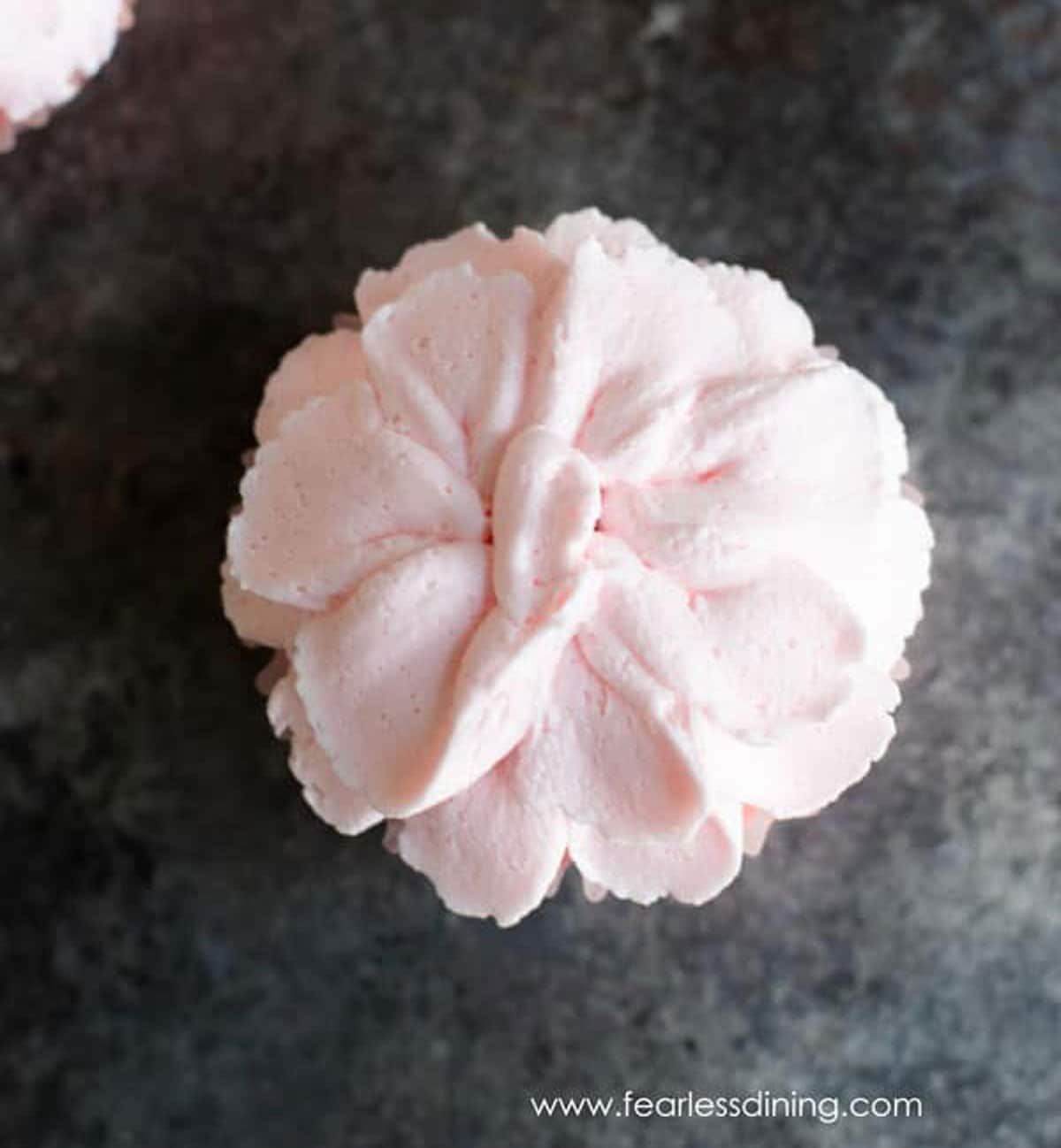 The top view of a pink flower frosting topped cupcake.