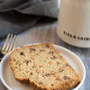 a slice of zucchini bread on a plate next to a mug of coffee
