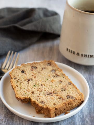 a slice of zucchini bread on a plate next to a mug of coffee