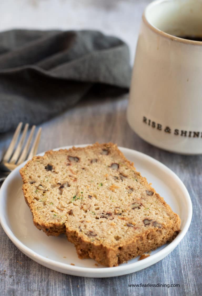 A slice of gluten free zucchini bread on a plate next to a mug of coffee.