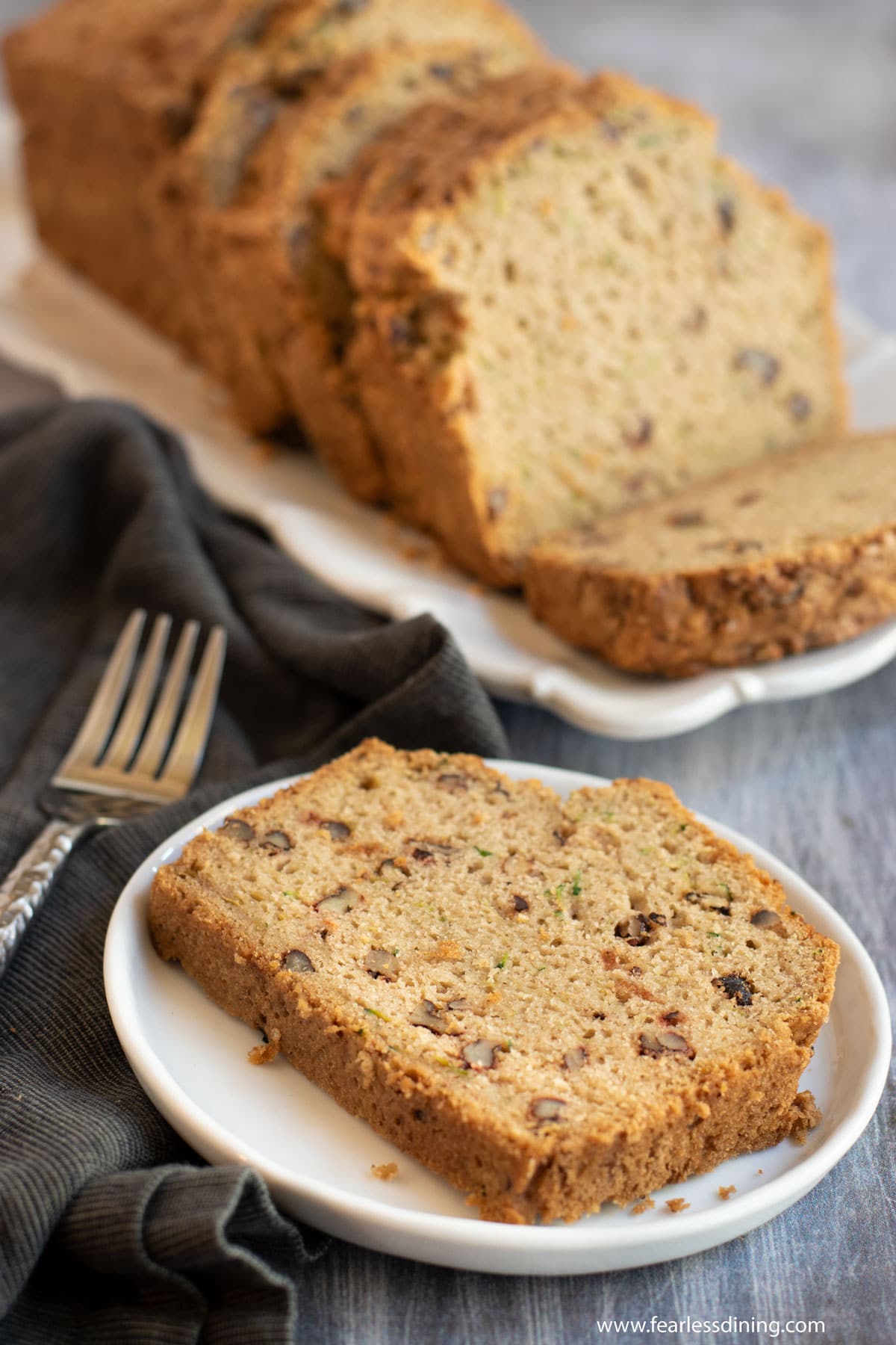 A slice of zucchini bread on a plate next to the loaf.