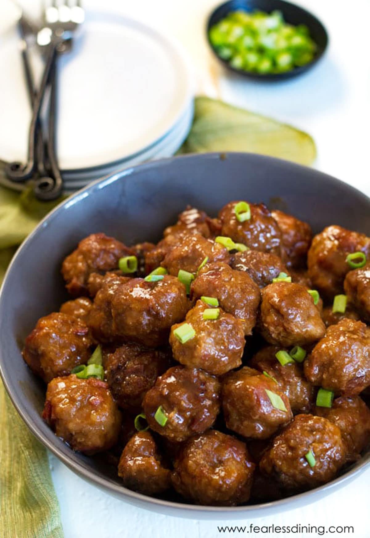 A large grey bowl full of meatballs. They are garnished with scallions.