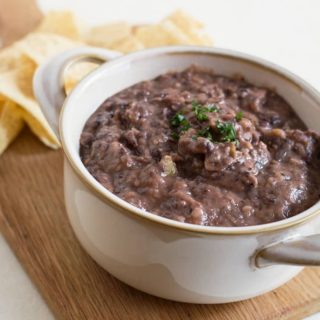 A bowl full of black bean dip on a wooden serving tray.