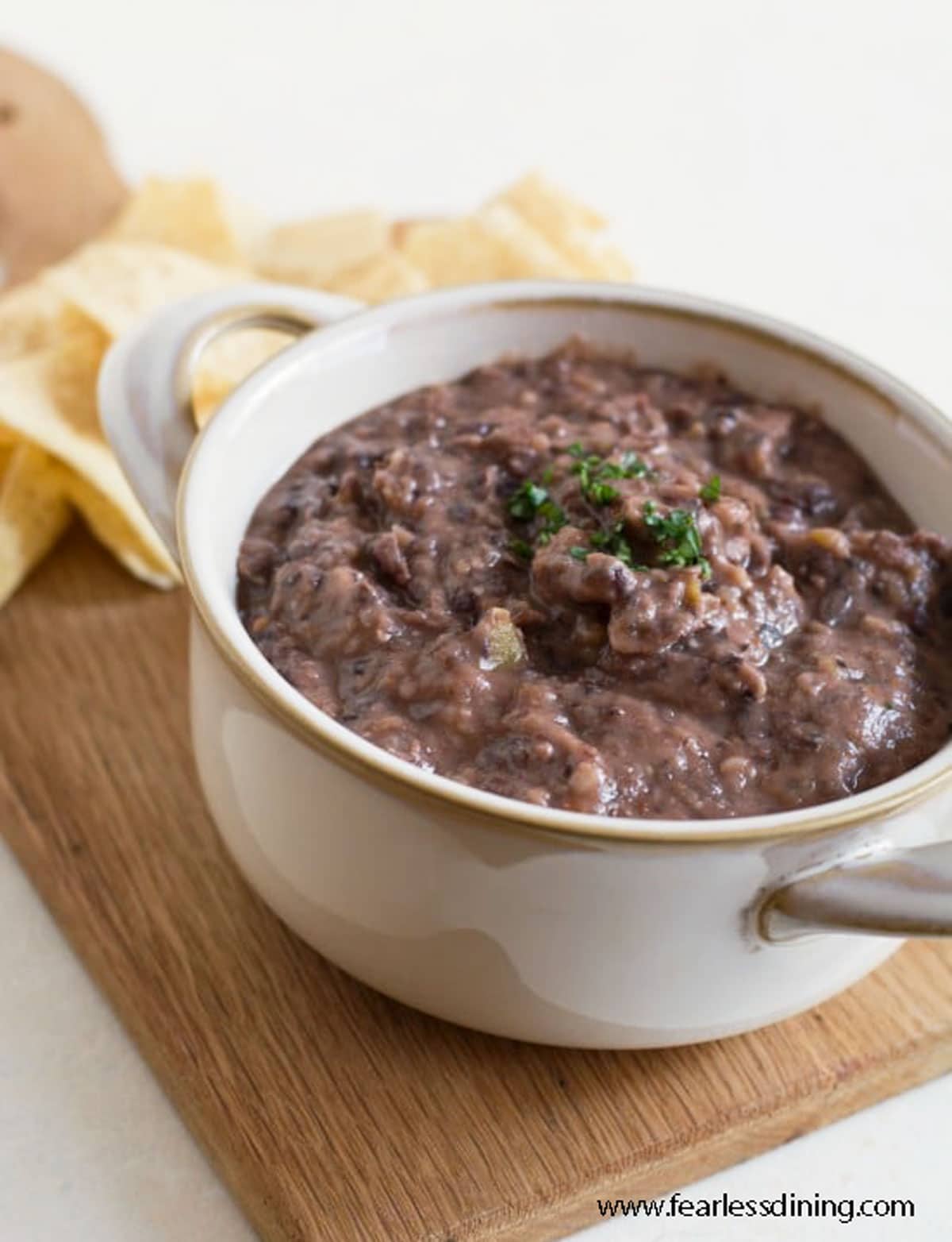 A bowl full of black bean dip on a wooden serving tray.