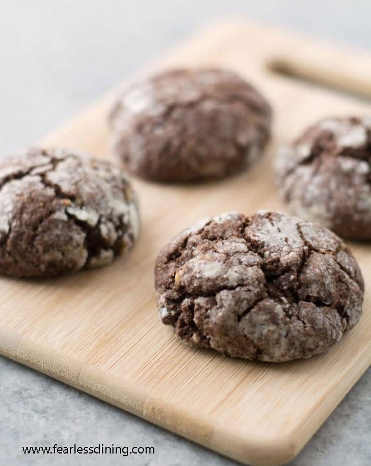 Baked gluten-free chocolate crinkle cookies on a wooden board.