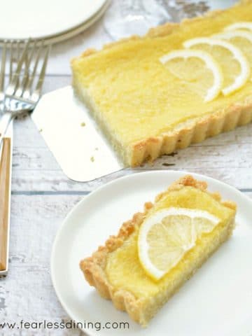 a slice of lemon tart on a white plate next to the whole tart