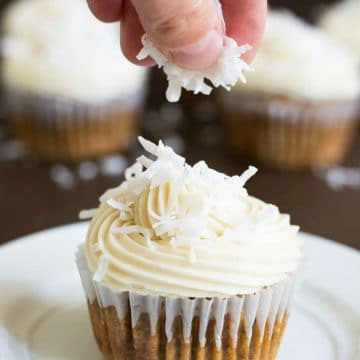 Sprinkling shredded coconut over a gluten free carrot cake cupcake.