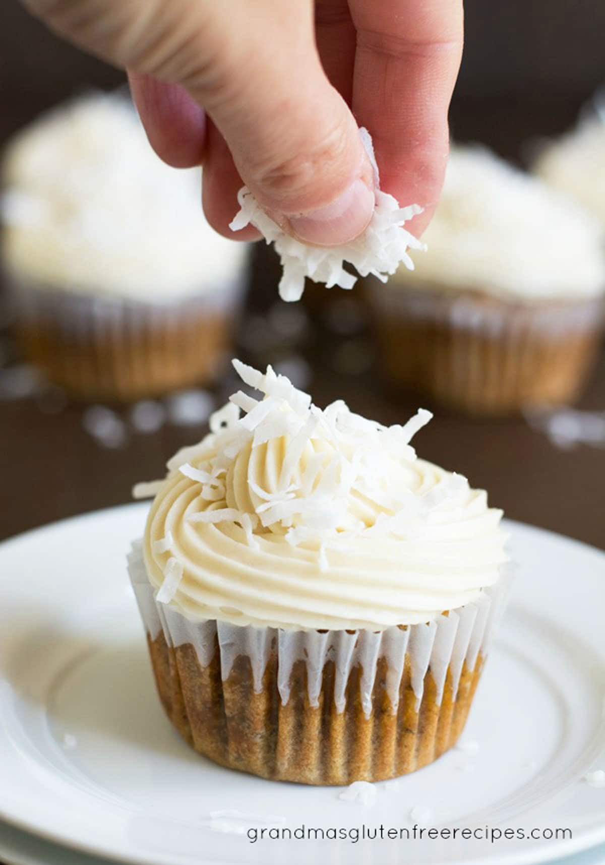 Sprinkling shredded coconut over a cupcake.