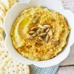 A bowl of hatch chile hummus next to crackers.