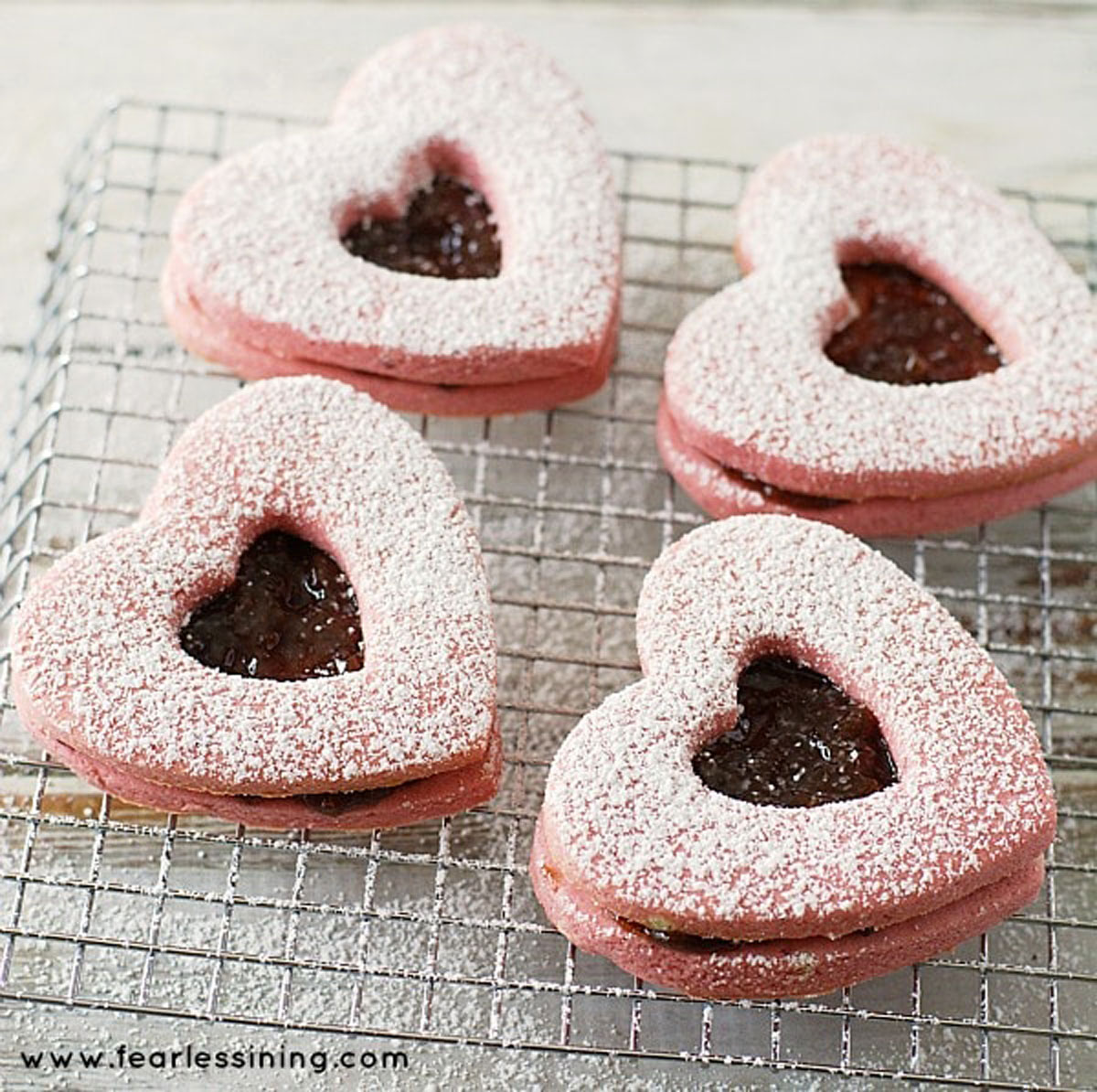 Powdered sugared dusted linzer cookies on a rack.