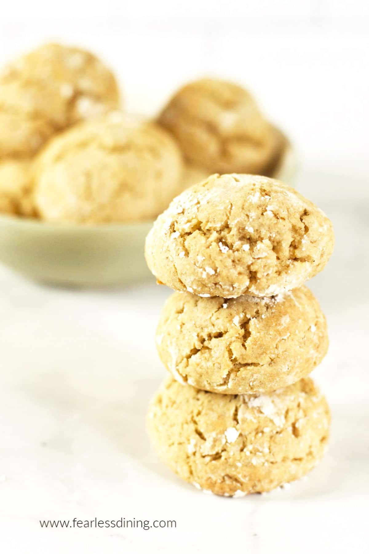 A stack of honey cookies next to a bowl of cookies.