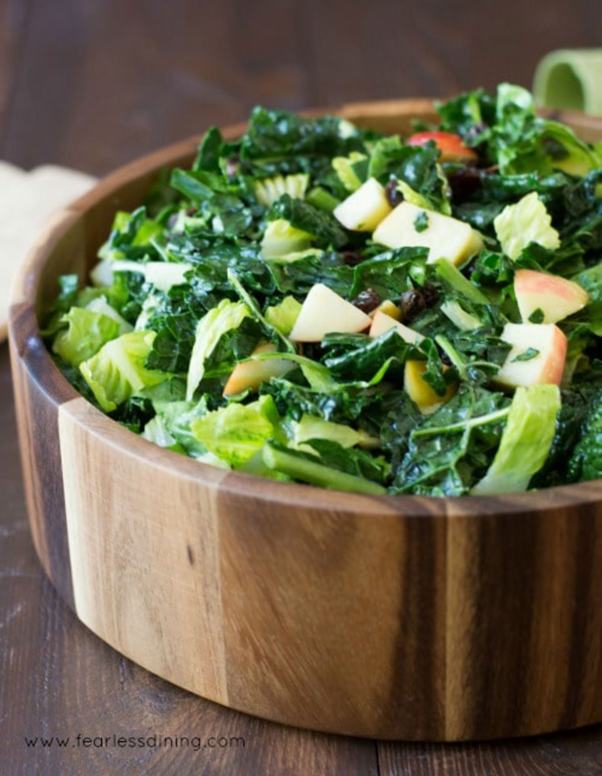 the side view of a big wooden bowl filled with kale salad.