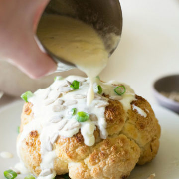 Pouring alfredo sauce on roasted cauliflower.