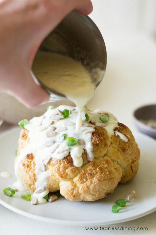 Pouring alfredo sauce on roasted cauliflower.