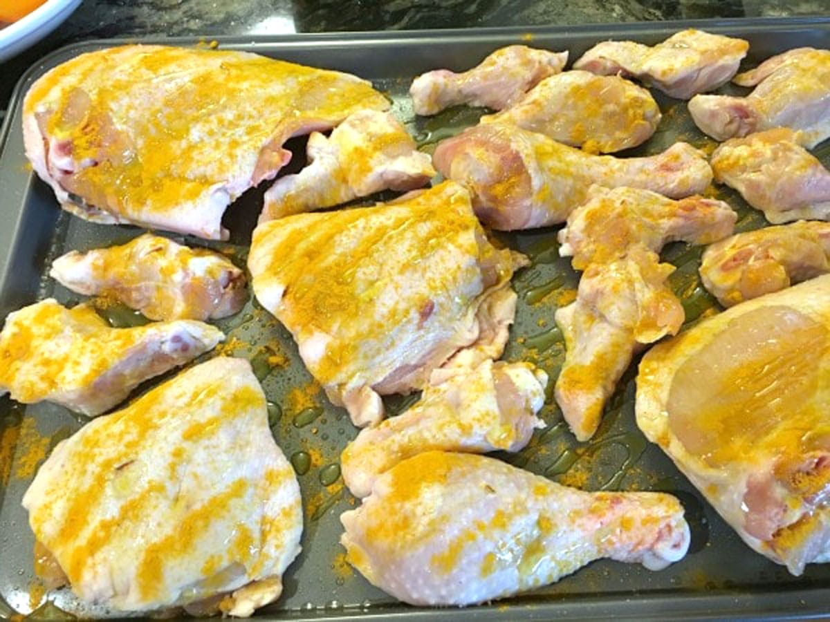 Chicken coated in turmeric and oil on a baking pan ready to bake.