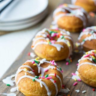 Vanilla donuts with icing and rainbow sprinkles on a cutting board.