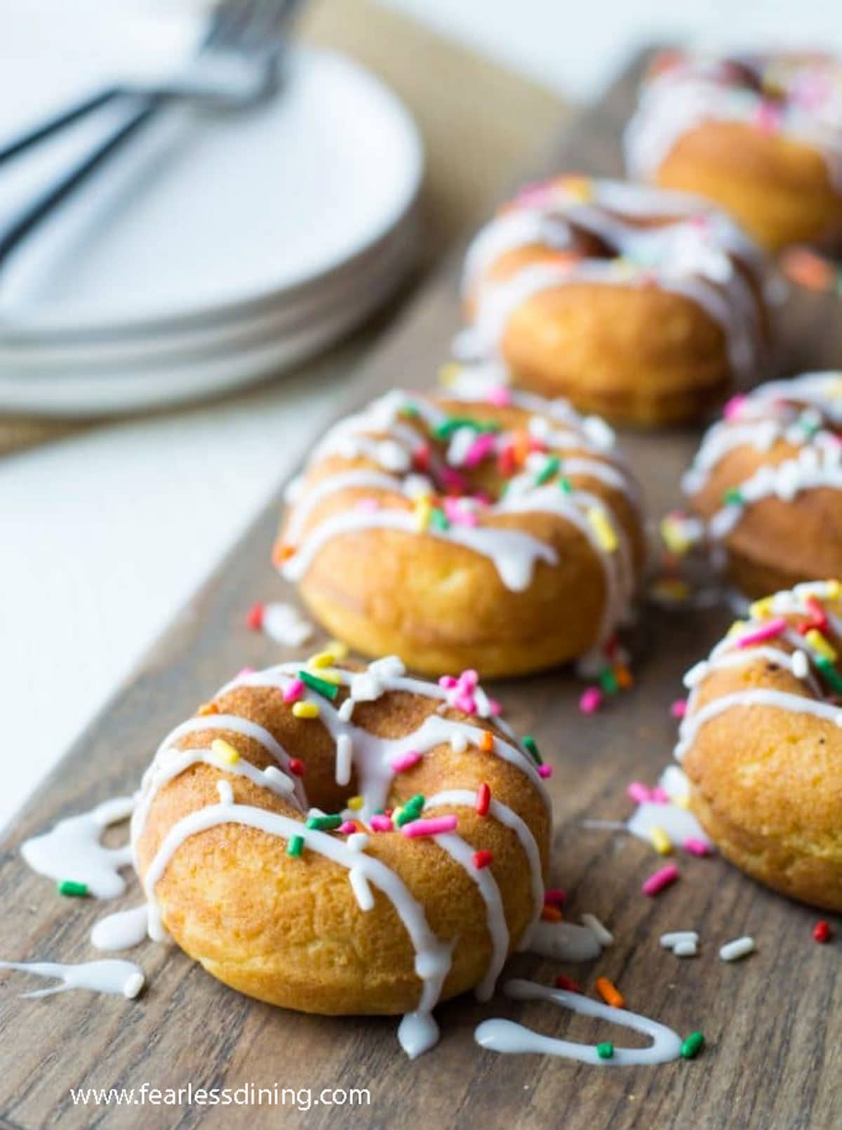 The vanilla donuts with icing and rainbow sprinkles on a cutting board.
