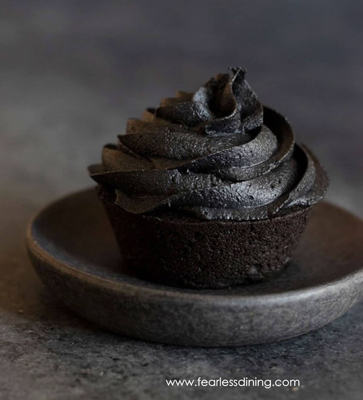 a close up of a black cupcake on a charcoal grey plate.