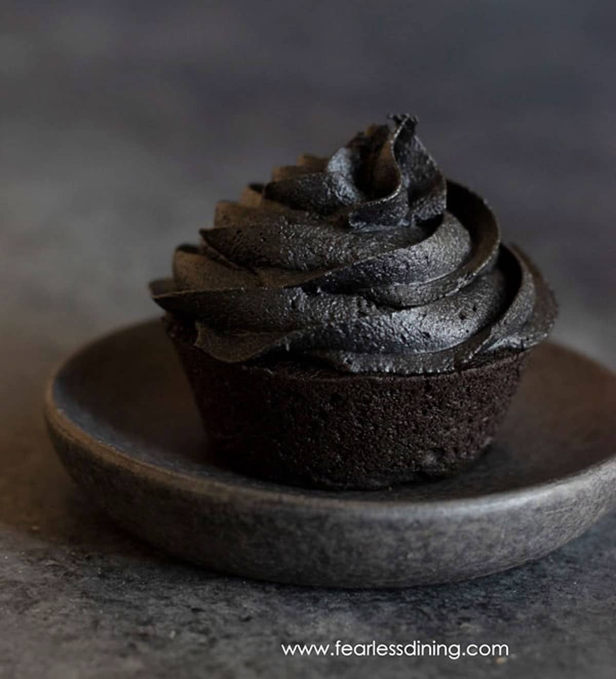 A close up of a black cupcake on a charcoal grey plate.