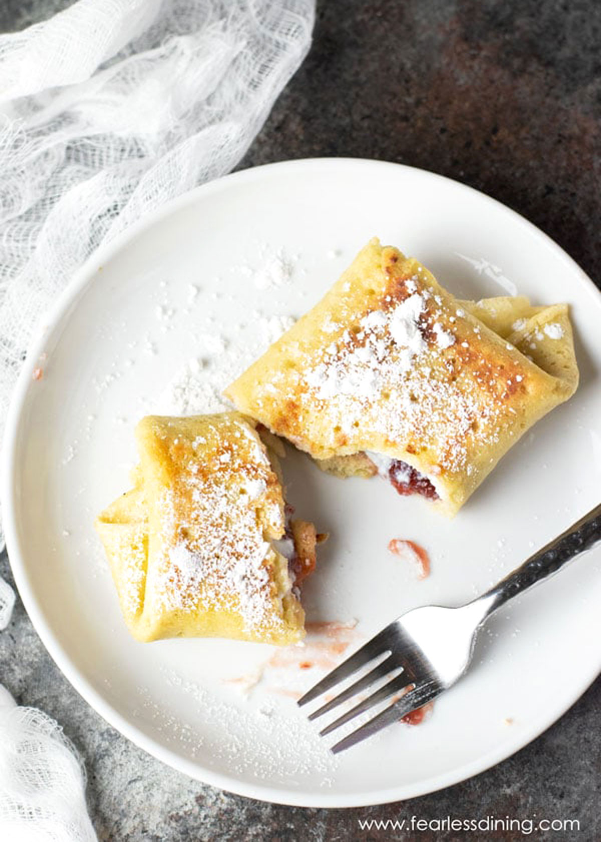 A cheese blintz cut on a plate. It was dusted with powdered sugar.