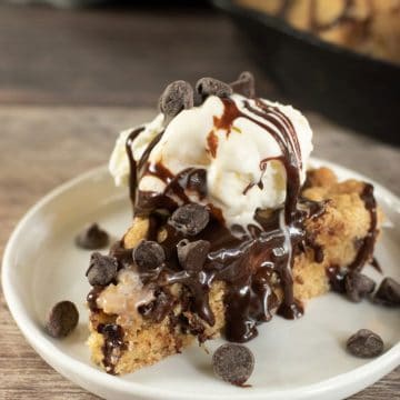 A slice of skillet cookie topped with ice cream an hot fudge.