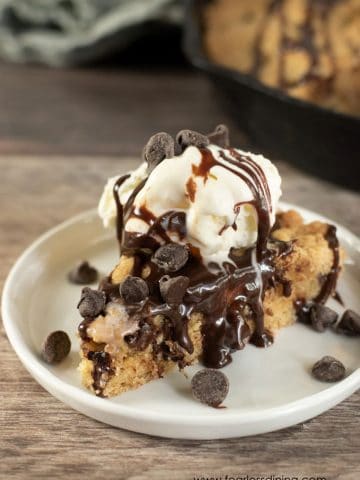 A slice of skillet cookie topped with ice cream an hot fudge