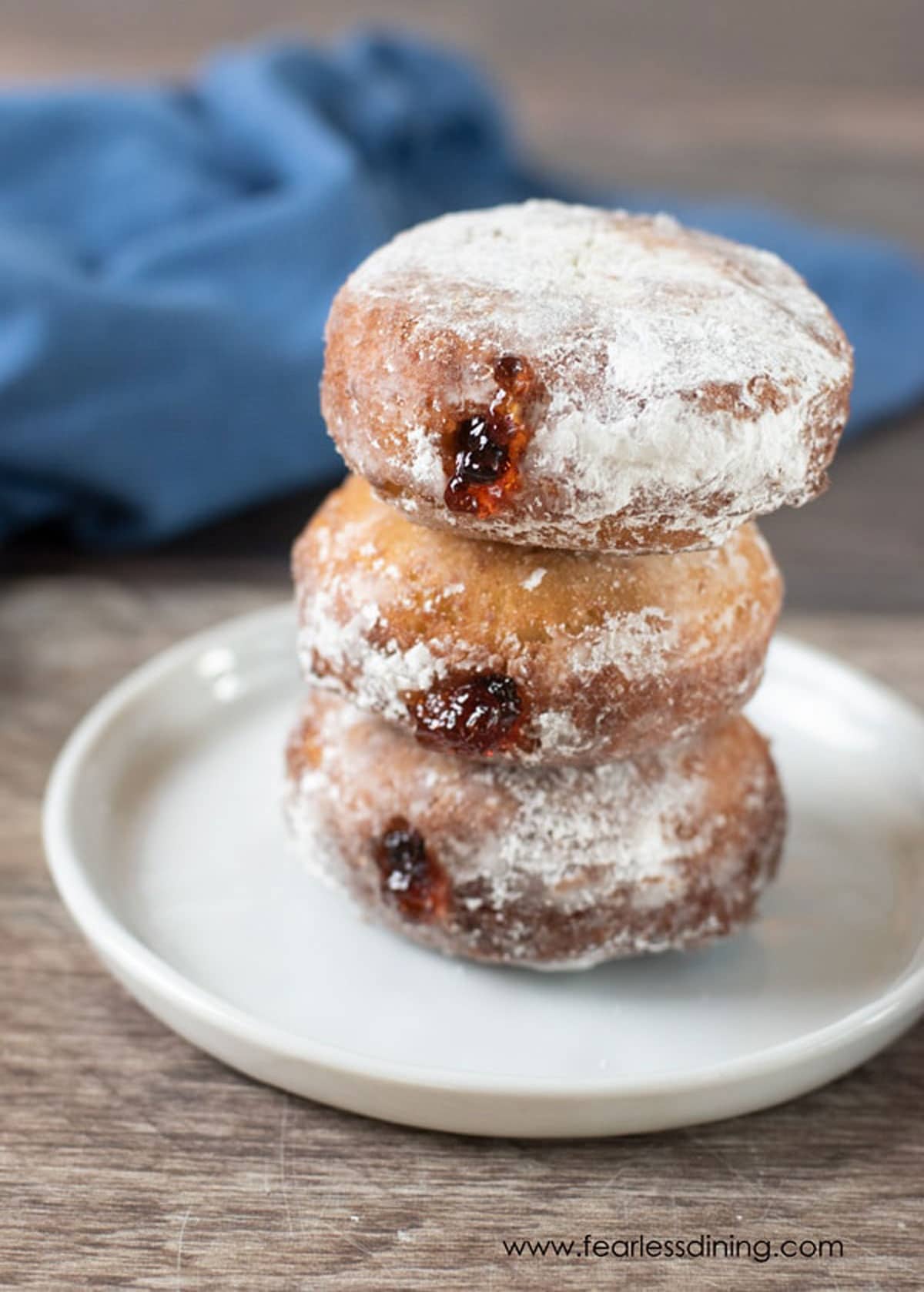 A stack of three jelly donuts on a plate.