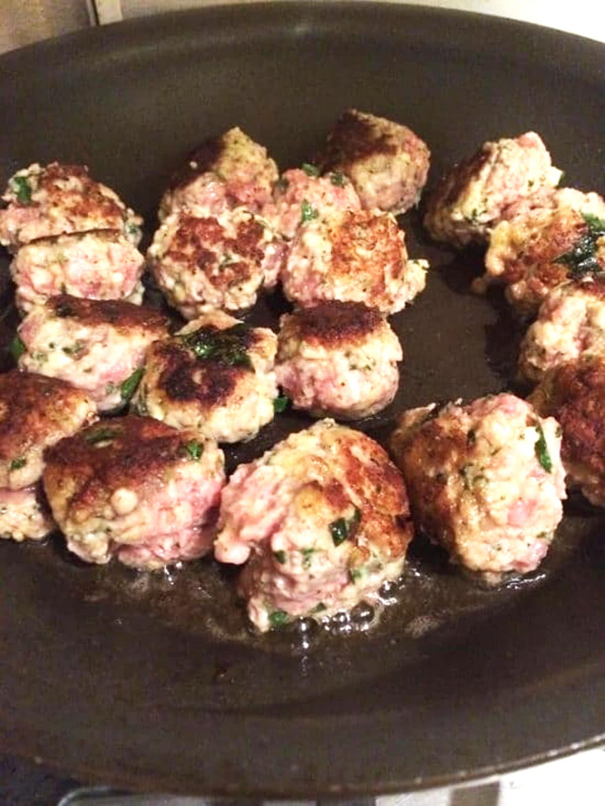 Meatballs cooking in a cast iron skillet.