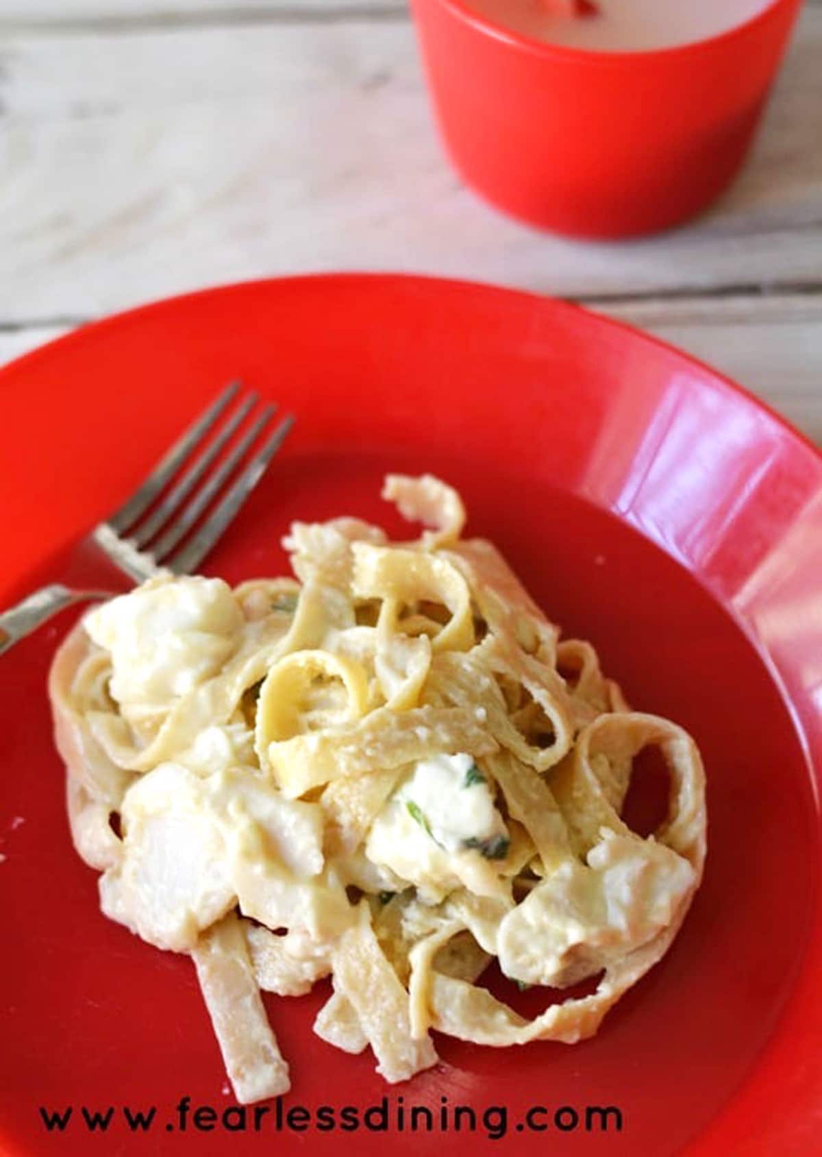 A serving of cod alfredo on a red plastic kid's plate.