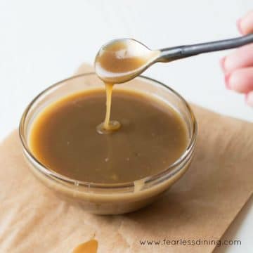 A glass bowl filled with butterscotch sauce. A spoon is drizzling sauce into the bowl.