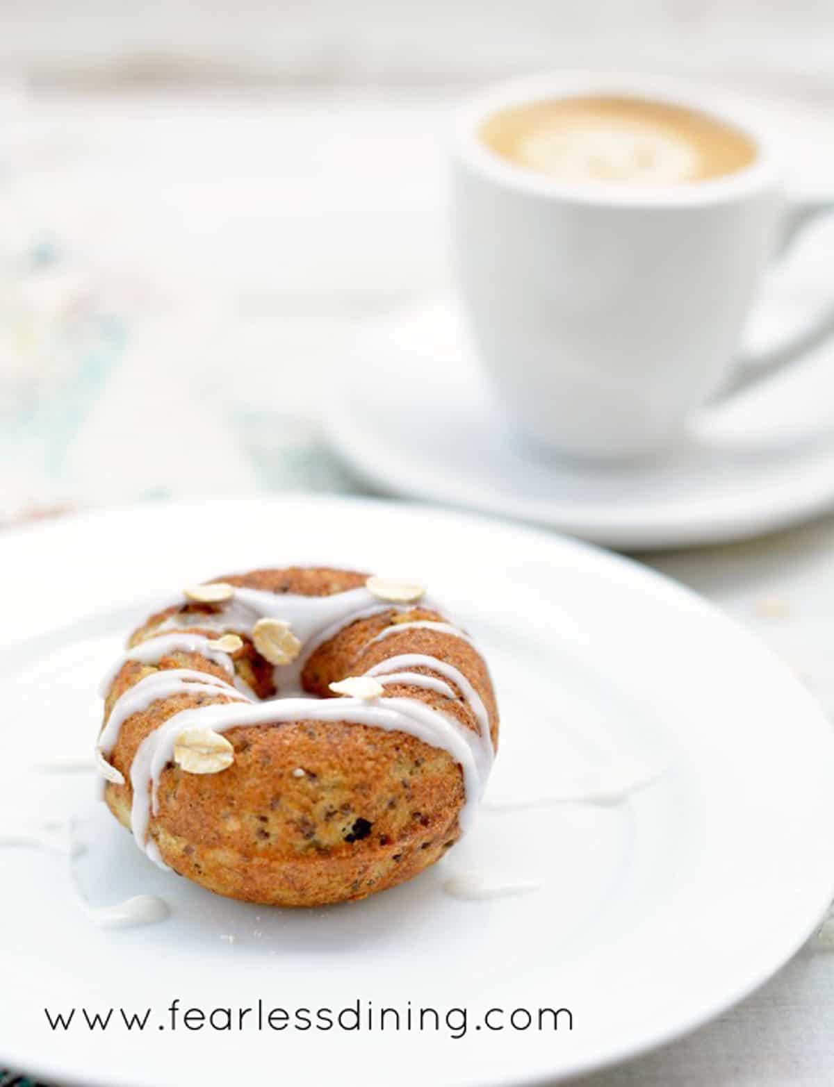 A mini donut with icing on a small white plate.