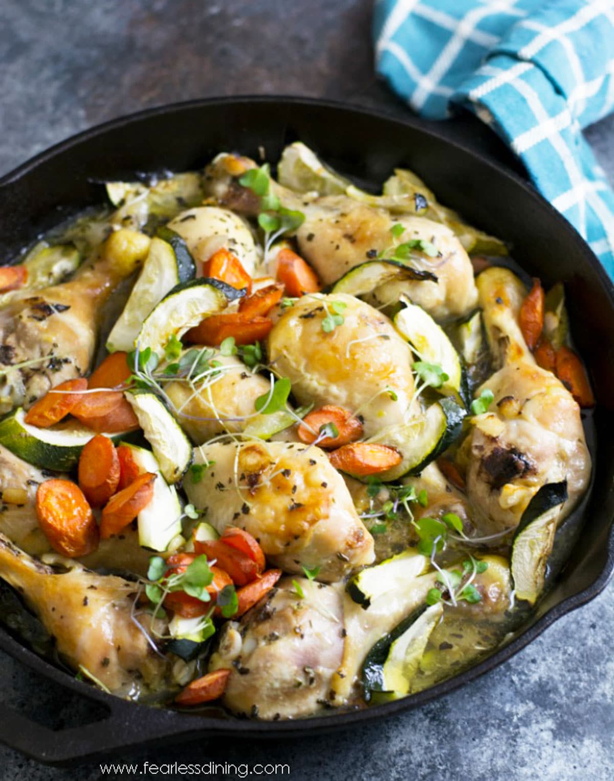 Acast iron skillet with cooked chicken legs and vegetables.