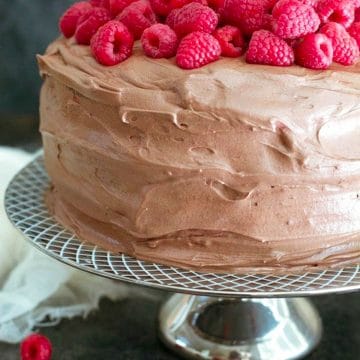 A frosted gluten free chocolate raspberry cake topped with fresh raspberries.