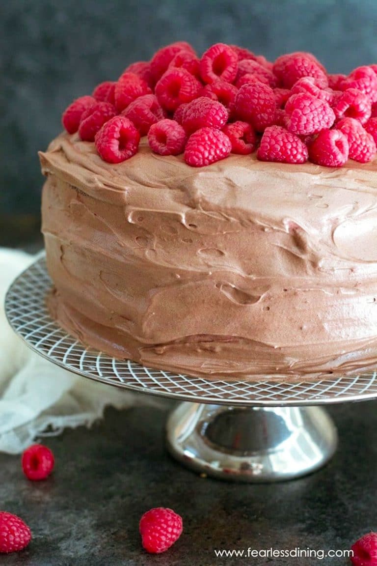 A frosted gluten free chocolate raspberry cake topped with fresh raspberries.