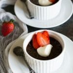 Two ramekins filled with chocolate custard. They are topped with whipped cream and sliced strawberries.