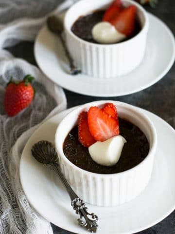 two ramekins filled with chocolate custard. They are topped with whipped cream and sliced strawberries