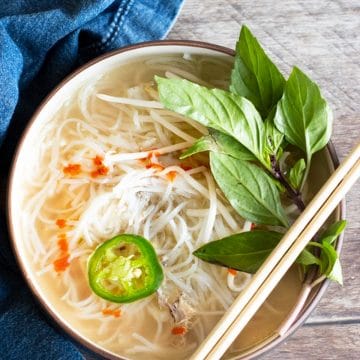 a top view of a big bowl of chicken pho. Chopsticks are resting on the lip of the bowl