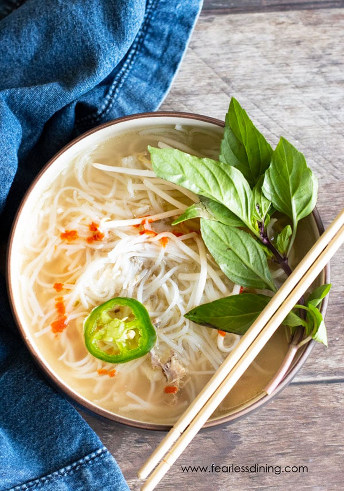 A top view of a big bowl of chicken pho. Chopsticks are resting on the lip of the bowl.