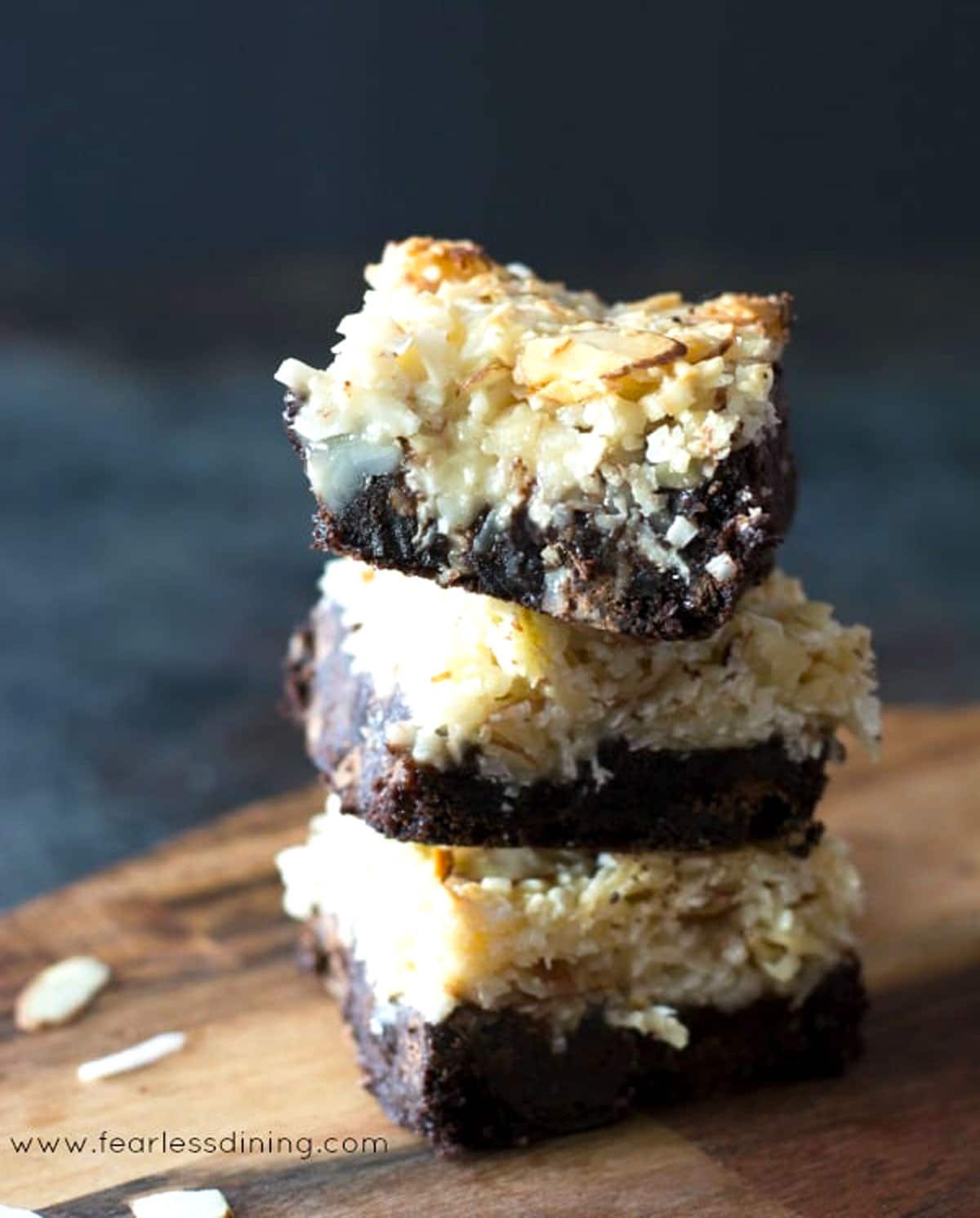A stack of three gluten free almond joy bars on a wooden cutting board.