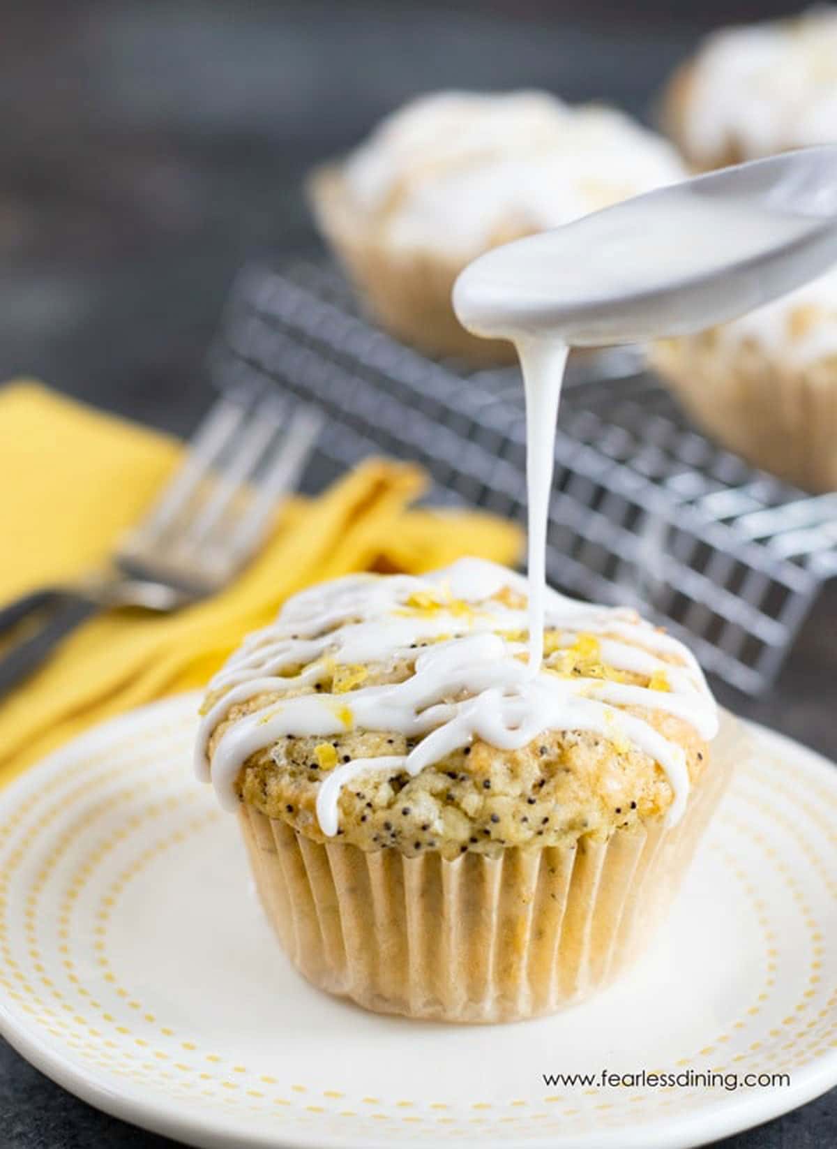 A spoon drizzling icing over a lemon poppy seed muffin.