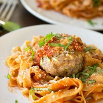 A plate with gluten free pasta with a large meatball on top.