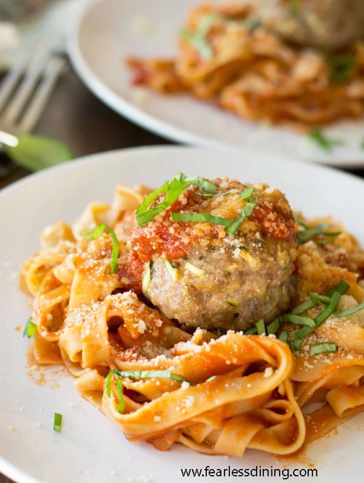A plate with gluten free pasta with a large meatball on top.