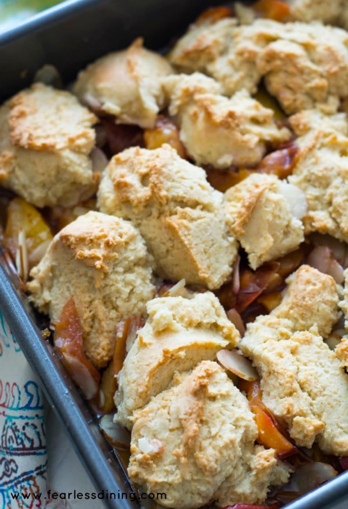 A pan full of baked peach cobbler with a golden biscuit topping.