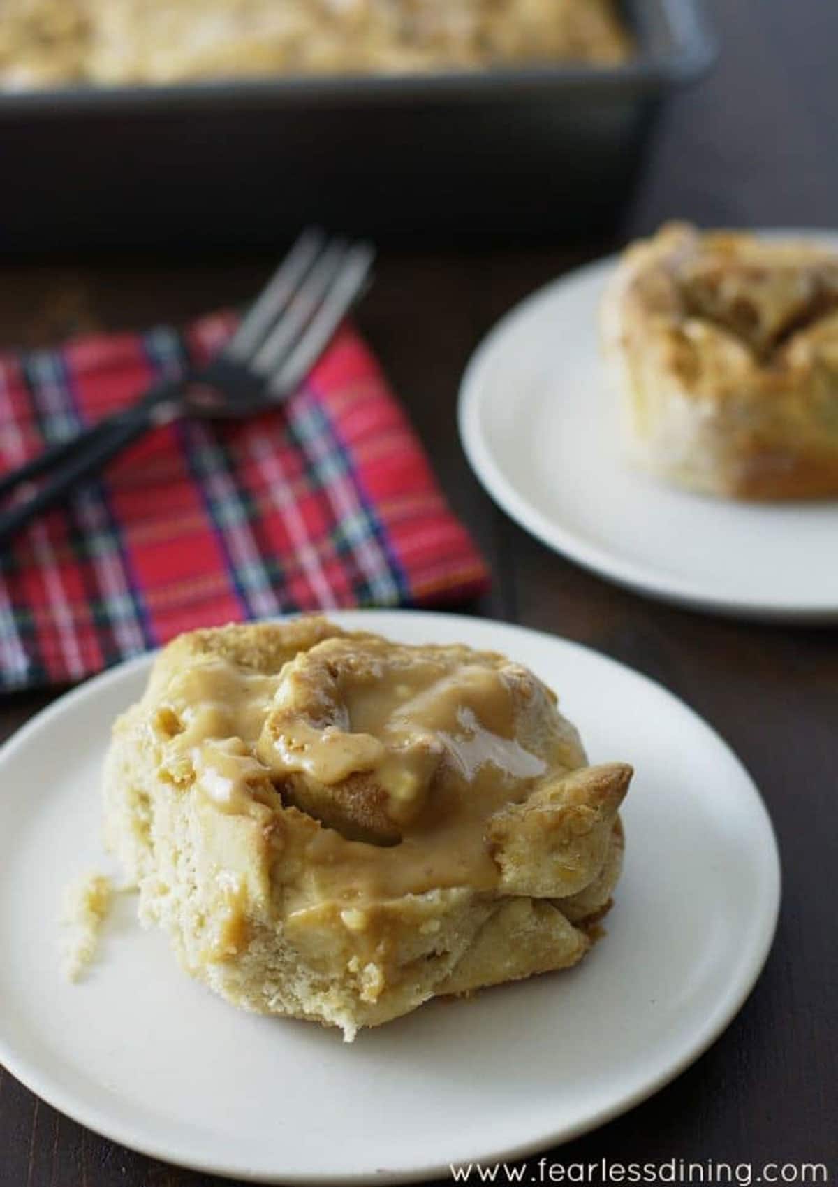 A peanut butter glazed cinnamon roll on a plate next to a plaid napkin.