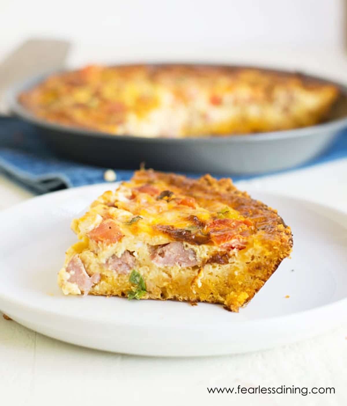 a slice of quiche on a white plate next to the pan