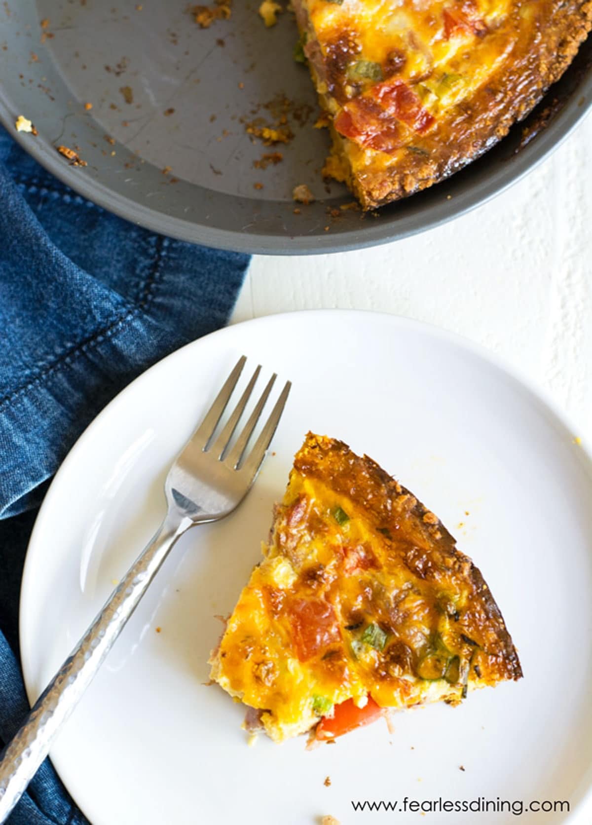 The top view of a slice of quiche on a plate next to the whole quiche.