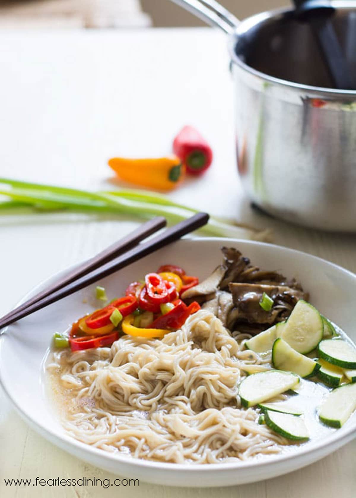 A bowl of gluten free ramen next to the pot of soup.