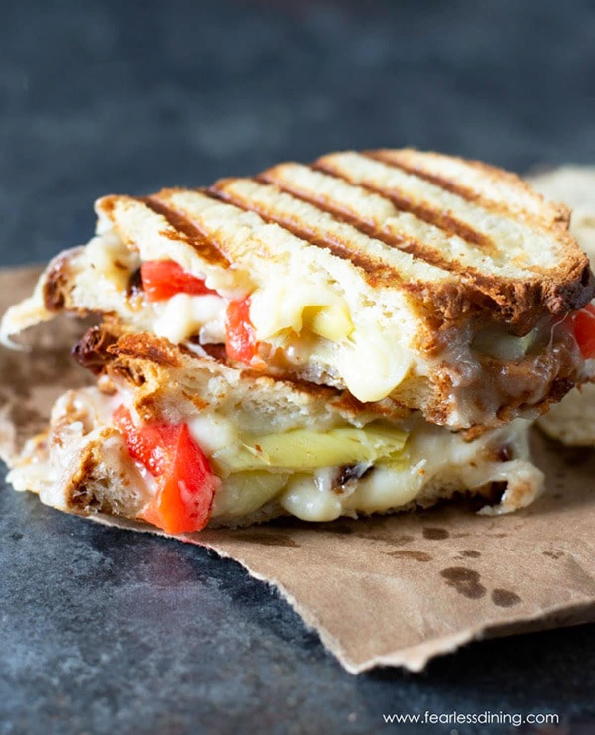 A gluten free Italian panini sandwich cut in half on a piece of paper.