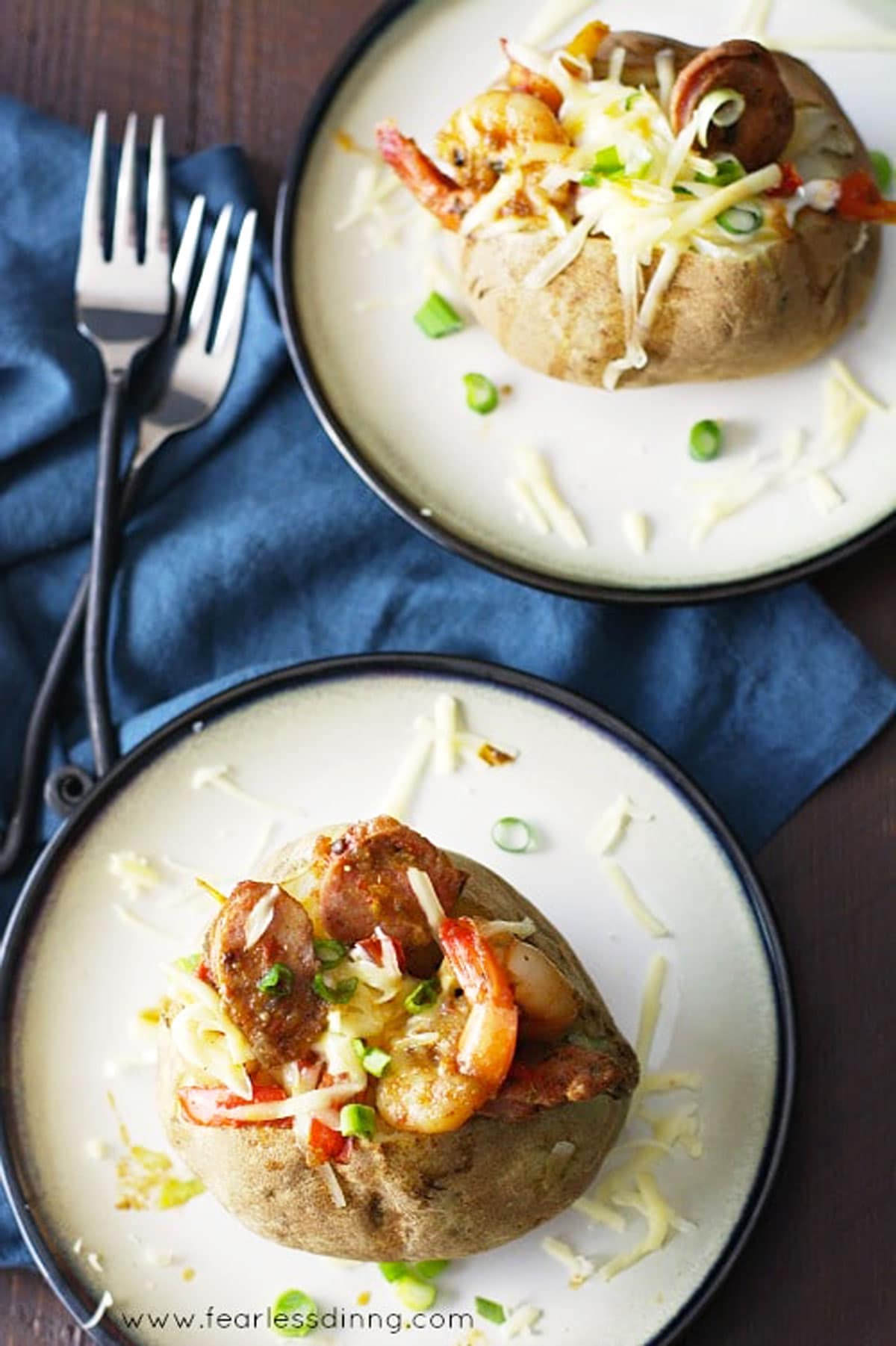 The top view of two jambalaya stuffed baked potatoes on plates.